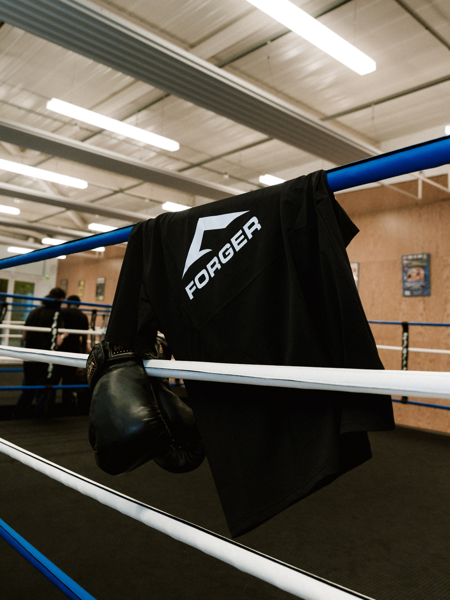 L'effort te forge — manifeste FORGER FORGER — t-shirt noir posé sur les cordes d'un ring de boxe avec gants d'entraînement, manifeste discipline et effort